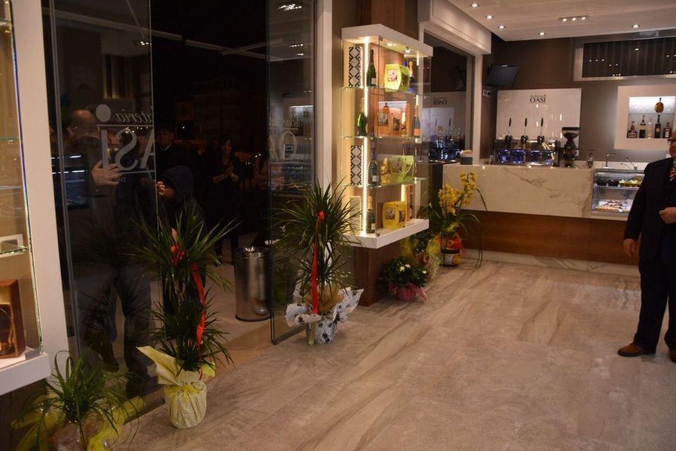 Ingresso di un negozio con porte in vetro, espositori, fiori e una persona in abito.