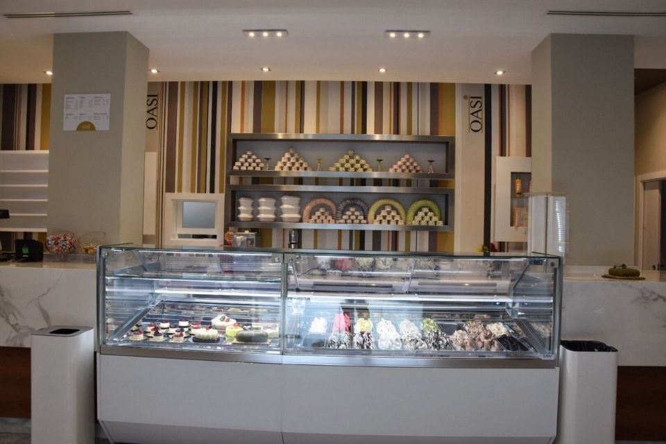 Vetrina per gelati in un negozio con vari gusti, ripiani in acciaio inox e sfondo a righe.