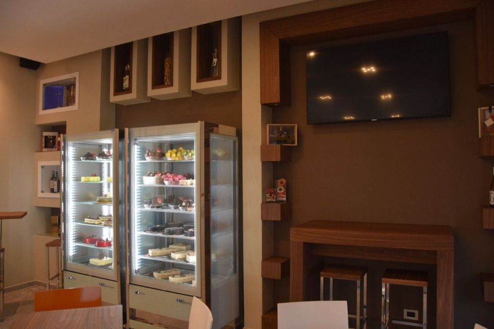 Interno di un bar con espositori di dolci, TV e posti a sedere. Combinazione di colori marrone e bianco.