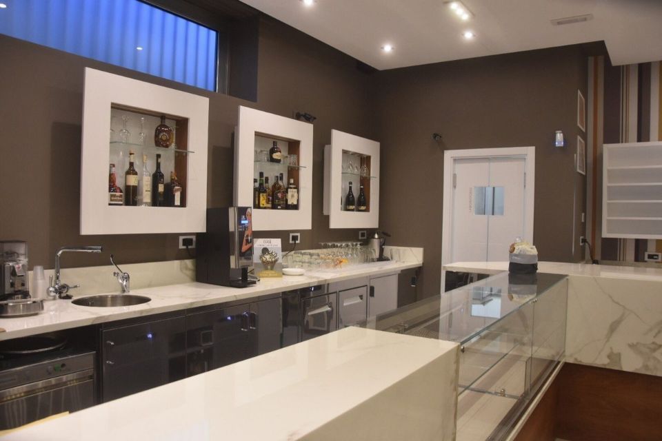 Zona bar con bancone bianco, pareti marroni e mensole espositive incassate per le bottiglie.