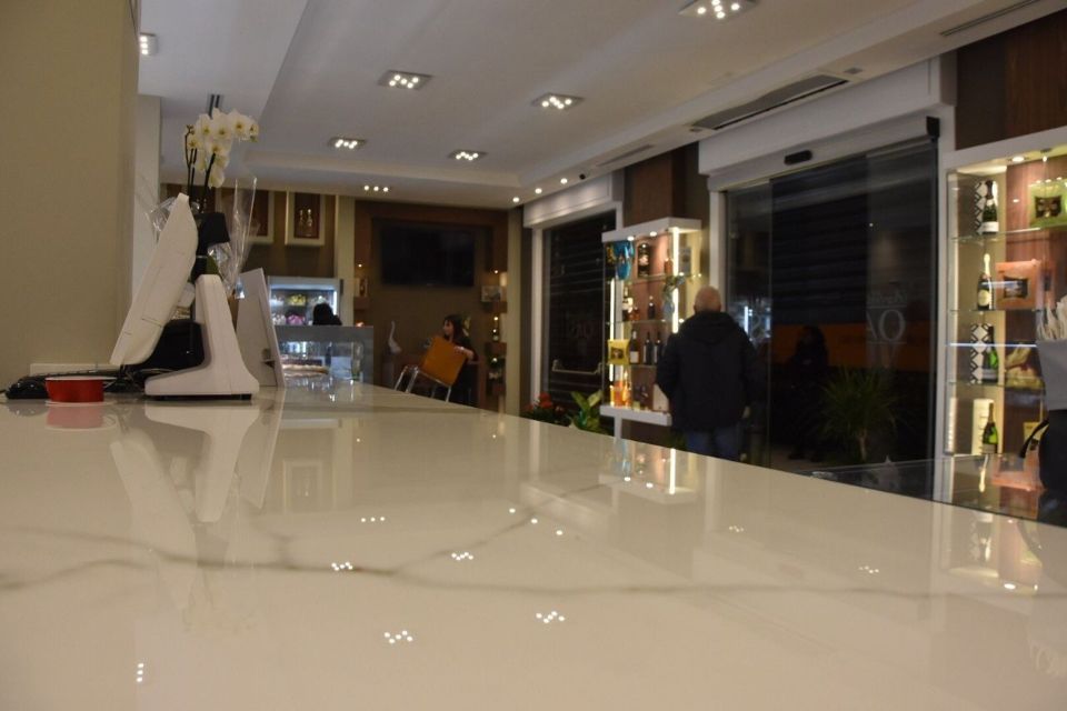 Interno di un negozio con un bancone luminoso. Una persona passa davanti a porte e vetrine in vetro.