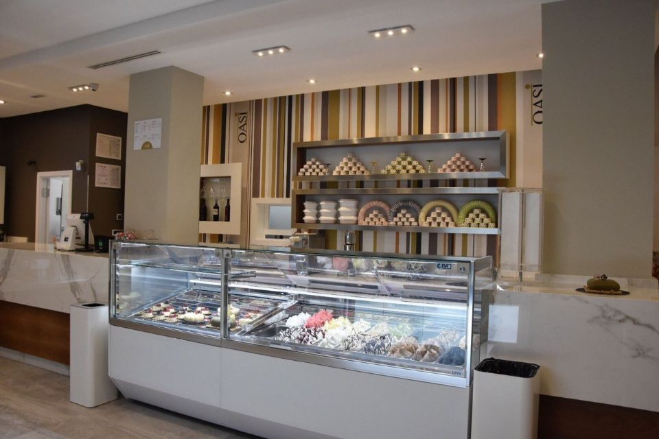 Interno di una gelateria con una vetrina piena di dolcetti colorati, scaffali di prodotti da forno e una parete decorativa.