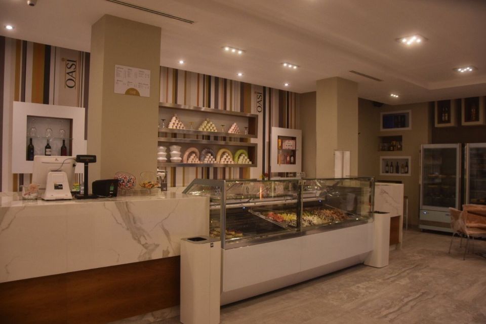 Interno di una gelateria con bancone in marmo, vetrina e parete a strisce.