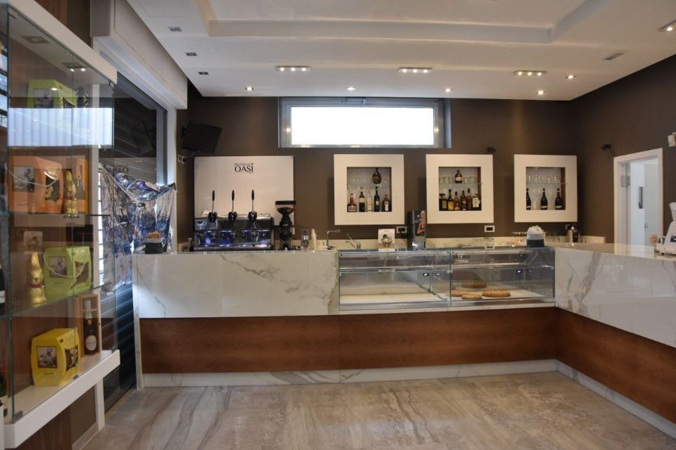 Interno di un bar con bancone in marmo, macchina per l'espresso, vetrine e pareti marroni.