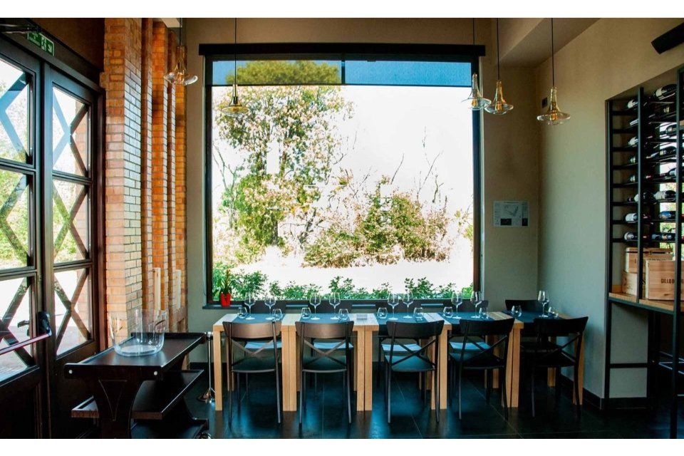 Zona pranzo con tavolo lungo, sedie nere, grande finestra con vista sul verde, pareti in mattoni e colori neutri.