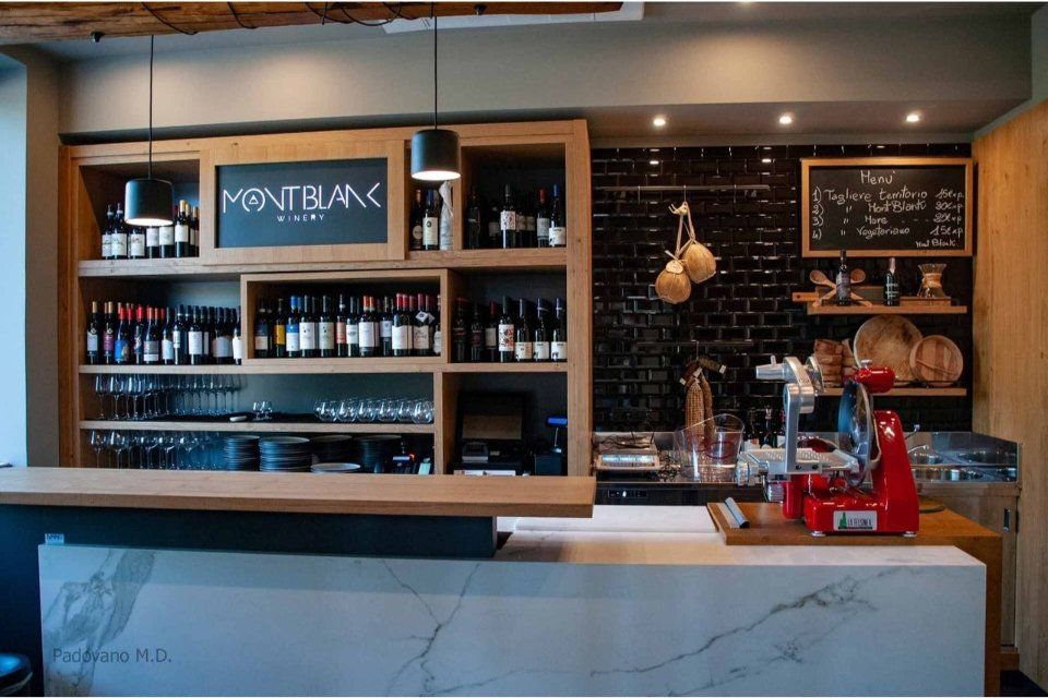 Vista interna di un bar con bottiglie di liquore sugli scaffali, un menù e un bancone in marmo.