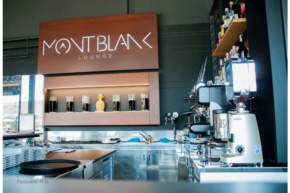 Bancone del bar Montblanc Lounge con macchina per caffè espresso, bottiglie e segnaletica in un ambiente moderno.