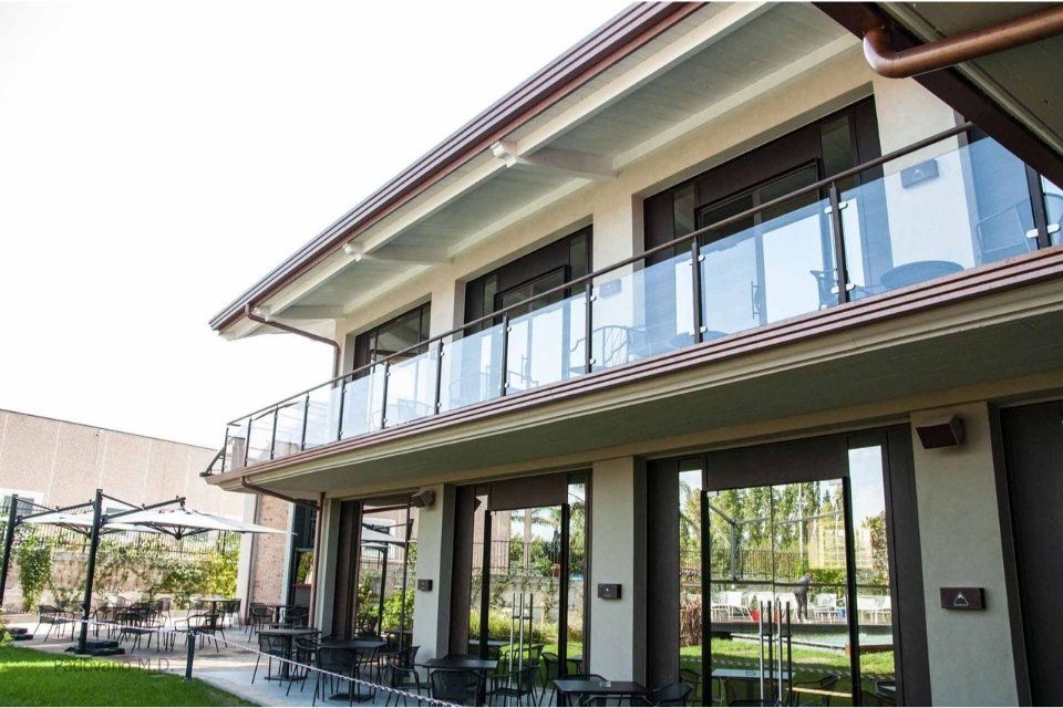 Edificio moderno con balconi in vetro, area salotto all'aperto, giornata soleggiata.