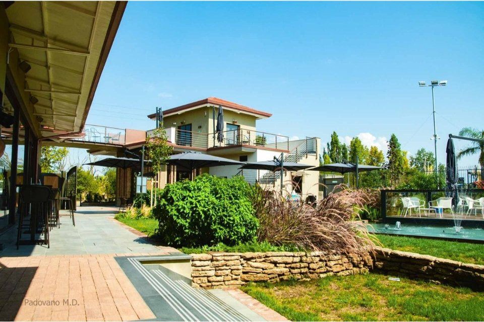 Esterno di un ristorante con posti a sedere all'aperto, patio in mattoni, prato e cielo soleggiato.