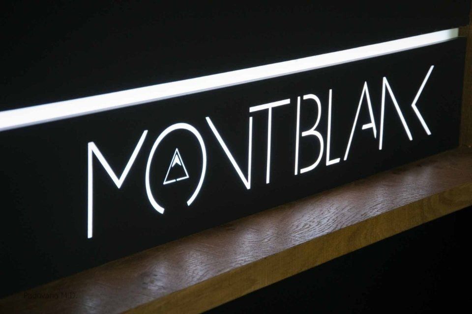 Insegna luminosa Montblanc con icona di montagna stilizzata in bianco su nero.