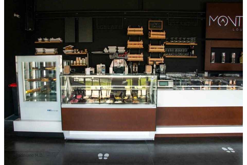 Bancone di una caffetteria con vetrine e scaffali contro una parete nera.