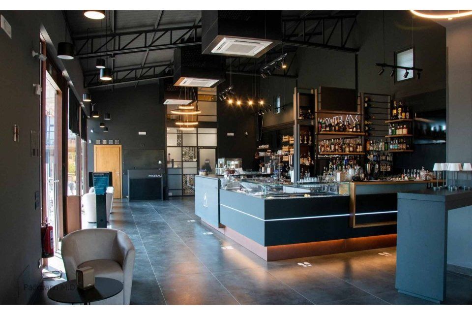 Interno di un bar moderno con pareti grigio scuro, bancone e illuminazione dall'alto.