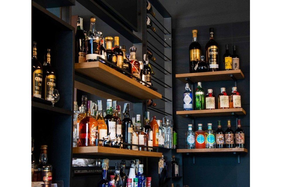 Scaffali con diverse bottiglie di liquore in un ambiente da bar. Scaffali scuri contro una parete scura.