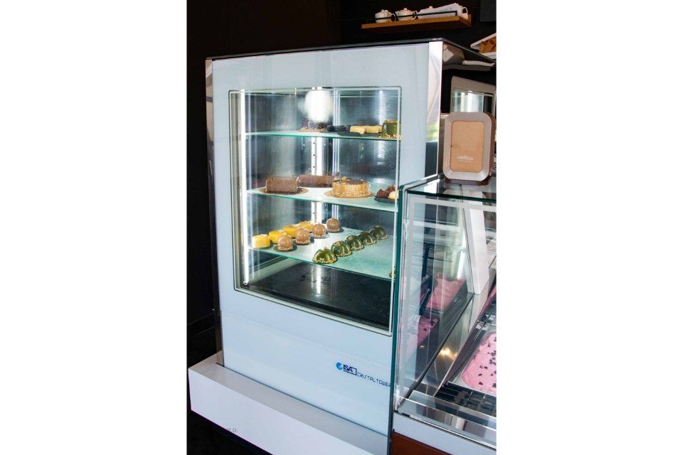 Vetrina con dolci in un bar. La vetrina è bianca con ripiani in vetro; i dolci sono visibili all'interno.