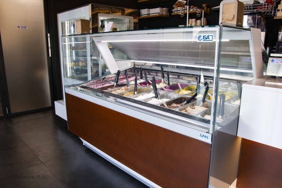 Vetrina gelato con vari gusti di gelato, bancone marrone e bianco.