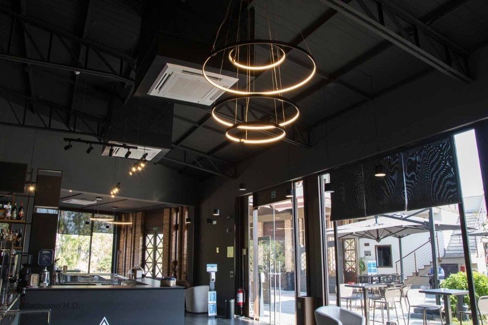 Interno di un moderno bar con pareti nere, grandi finestre e lampade a sospensione circolari.