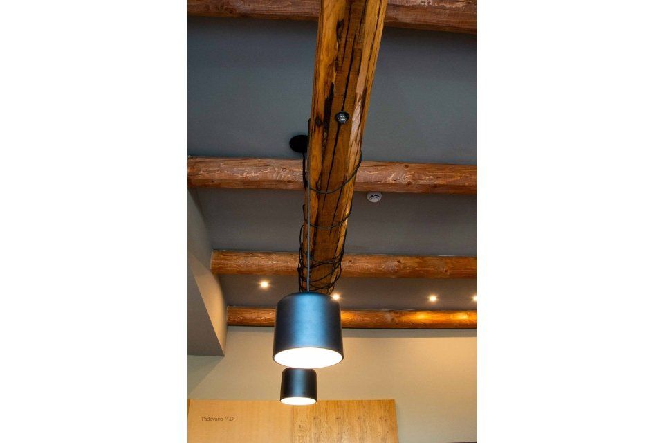 Lampade a sospensione cilindriche nere appese a un soffitto con travi in legno scuro.