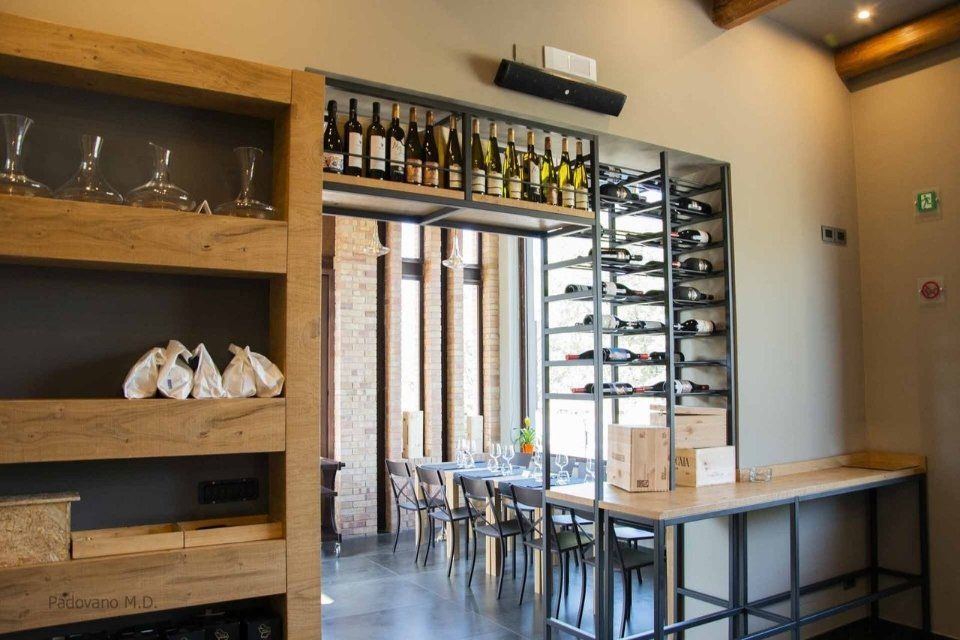 Interno di un ristorante con portabottiglie, scaffali e una zona pranzo visibile attraverso un'apertura.