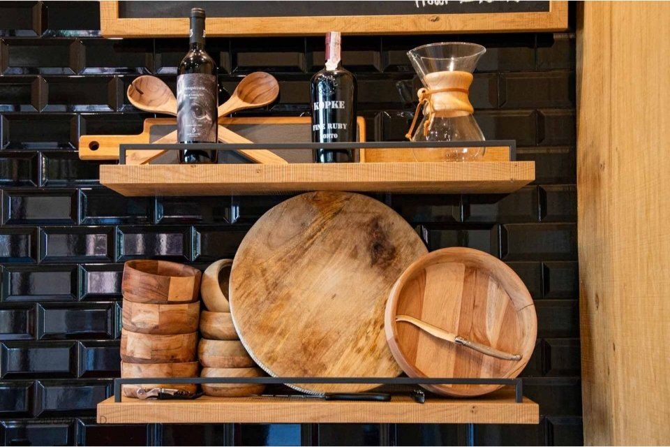 Scaffali in legno con utensili da cucina contro una parete piastrellata nera.
