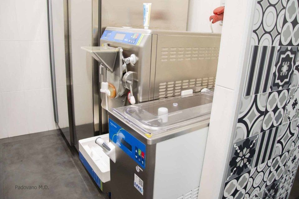 Macchina per gelato soft in un ambiente moderno. Acciaio inossidabile con display digitale, dettagli blu e piastrelle decorative.