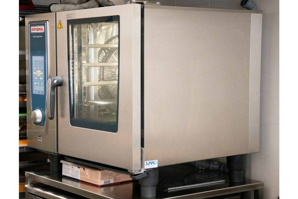 Grande forno commerciale in acciaio inossidabile in una cucina, appoggiato su un supporto.