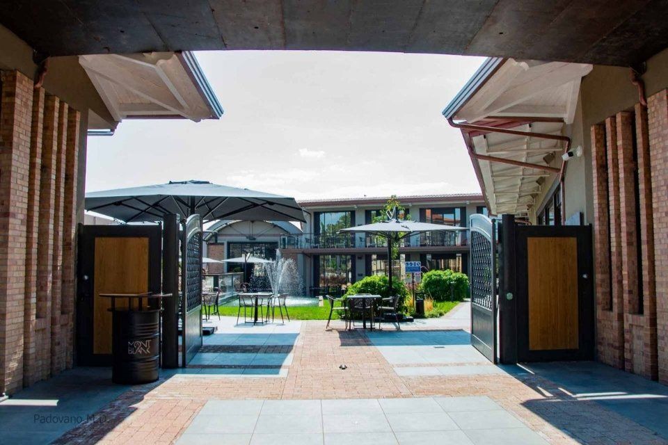 Cortile aperto con tavoli e ombrelloni, architettura in mattoni e legno, giornata di sole.