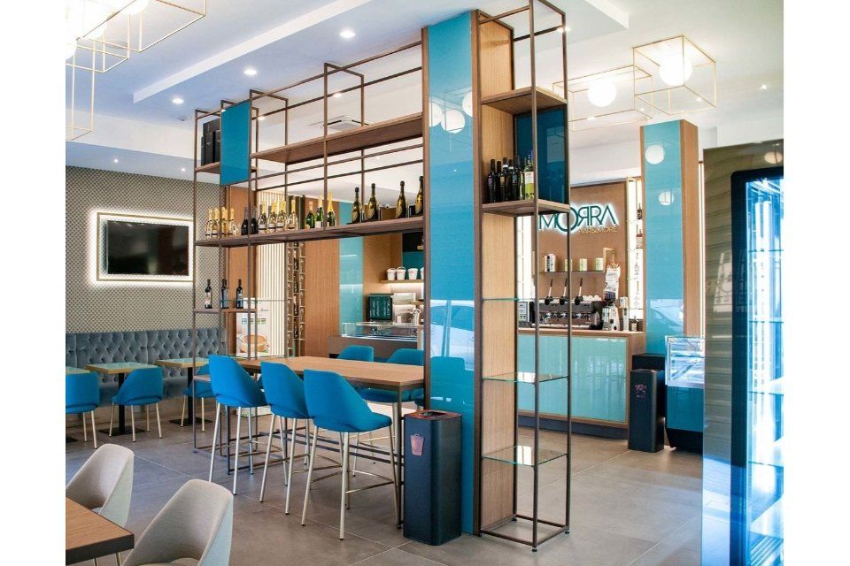 Interni del ristorante con dettagli color verde acqua e legno, posti a sedere al bar, scaffali con bottiglie.