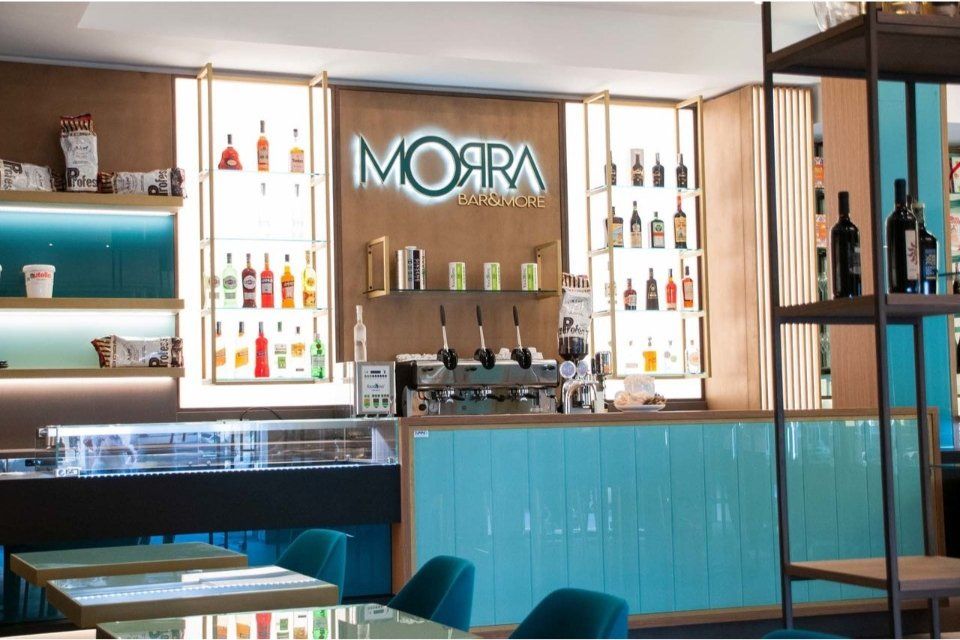 Interno del bar Morra con accenti turchesi e in legno, scaffali illuminati e bottiglie.