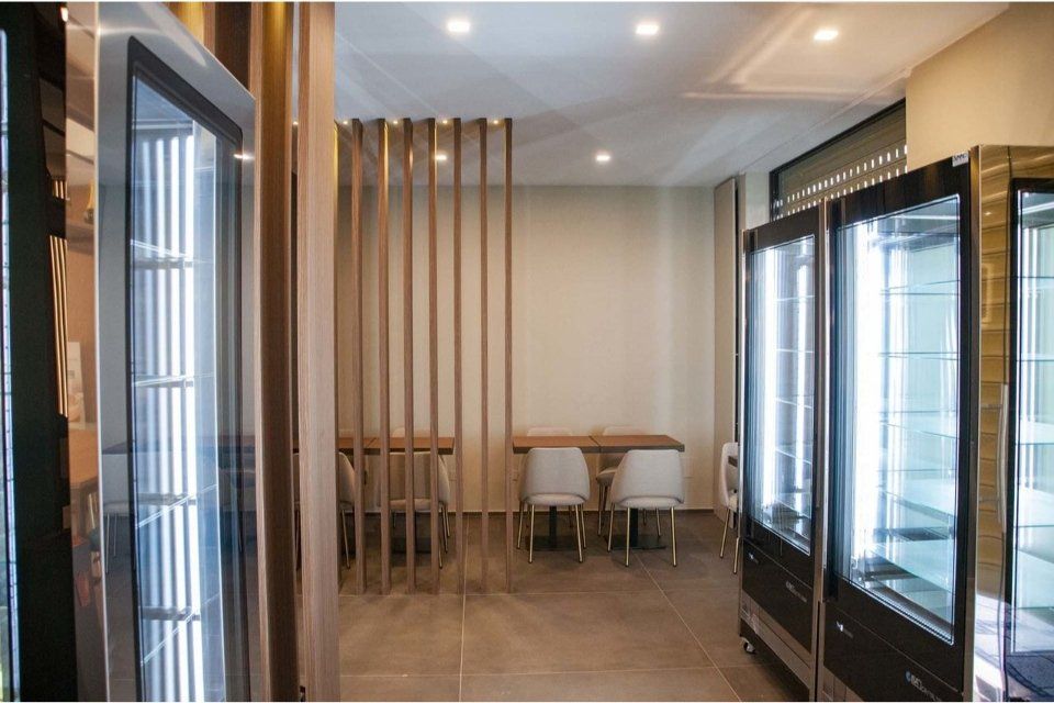 Vista interna di un negozio moderno con vetrine, dettagli in legno, sedute e illuminazione intensa.