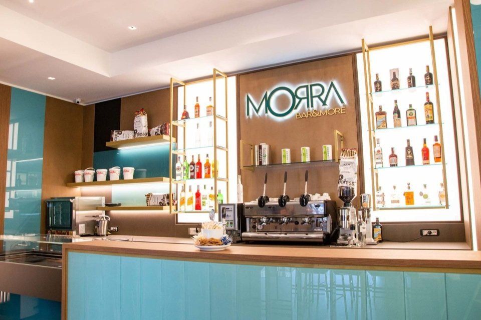 Bar con facciata in piastrelle color acquamarina e scaffali pieni di bottiglie e macchina del caffè, insegna