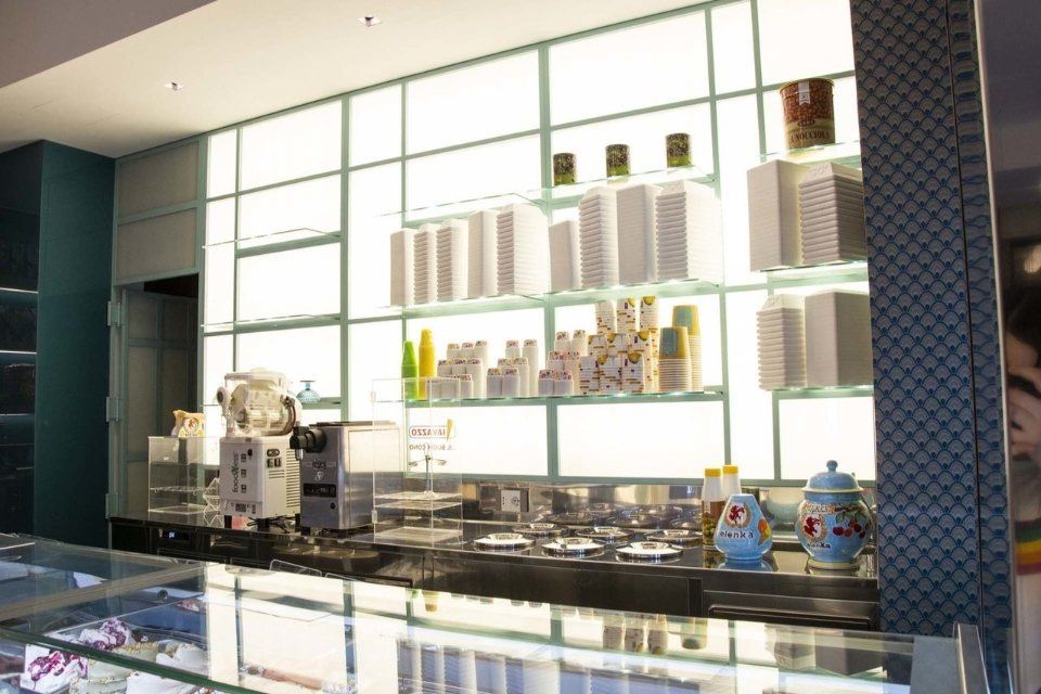 Un bar moderno e luminoso con scaffali illuminati su cui sono appoggiate tazze e contenitori dietro un bancone con le attrezzature.