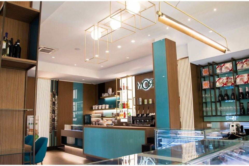 Interno di un bar con dettagli color verde acqua, un bar e scaffali con bottiglie di vino.