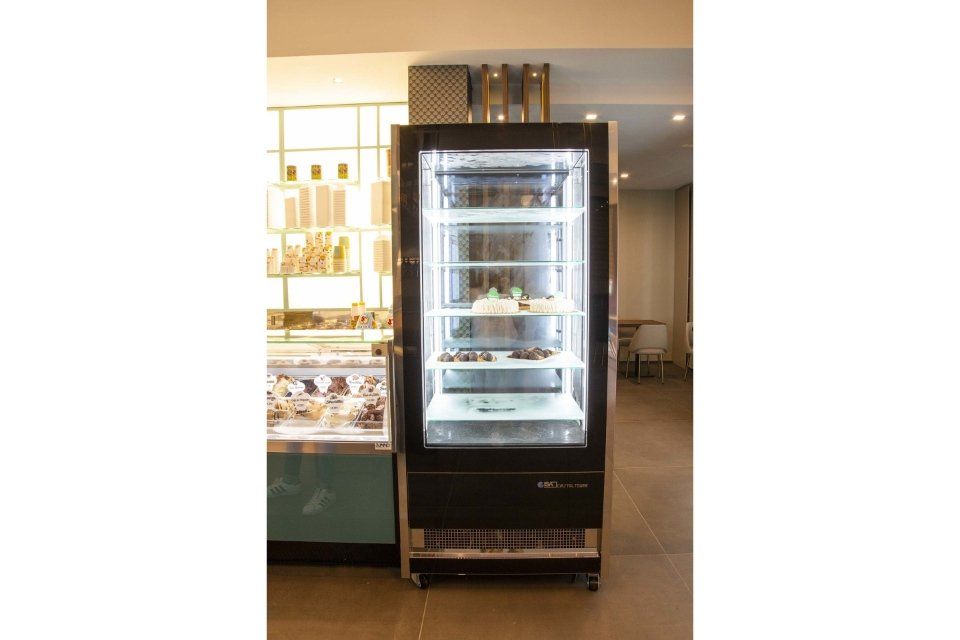 Frigorifero nero con esposizione di torte all'interno, in un ambiente da panetteria.