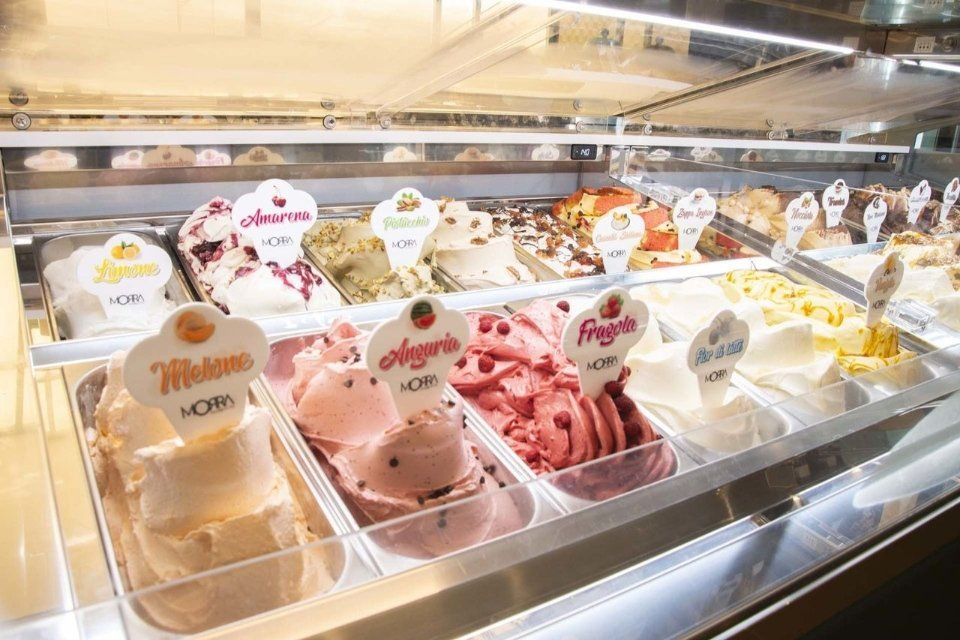 Vetrina per gelati con vari gusti colorati, tra cui rosa, bianco e giallo.