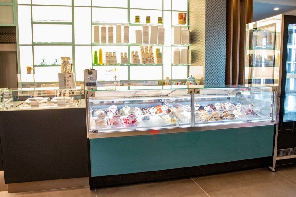 Interno di una gelateria con vetrina per il gelato, scaffali con prodotti e una parete turchese.