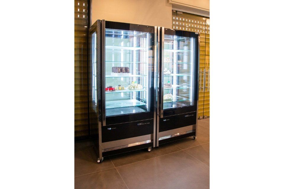 Due vetrine nere e argento con ante in vetro, che espongono pasticcini e dessert; ambiente interno.