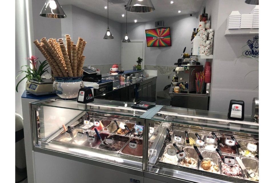 Interno di una gelateria con vetrina per il gelato, coni waffle e opere d'arte colorate.