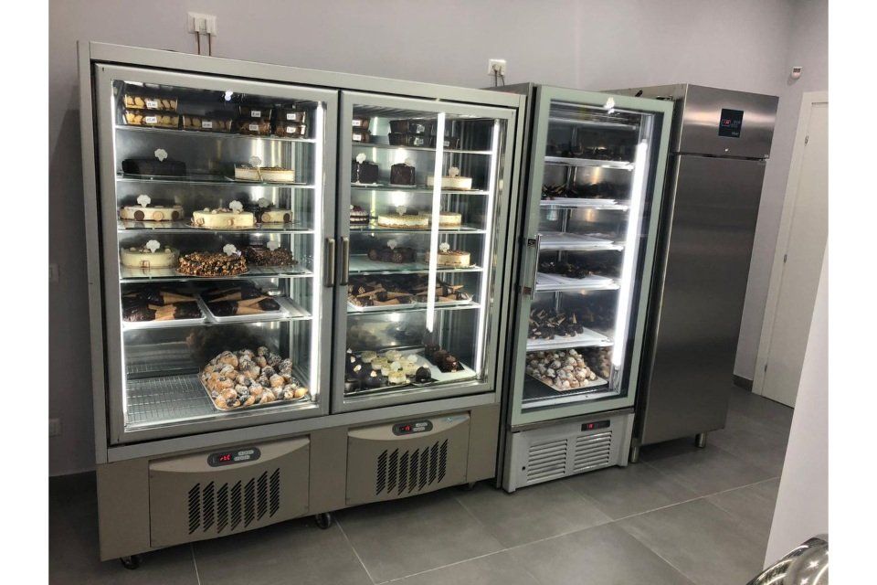 Vetrine con torte e pasticcini, accanto a un frigorifero, in un negozio.