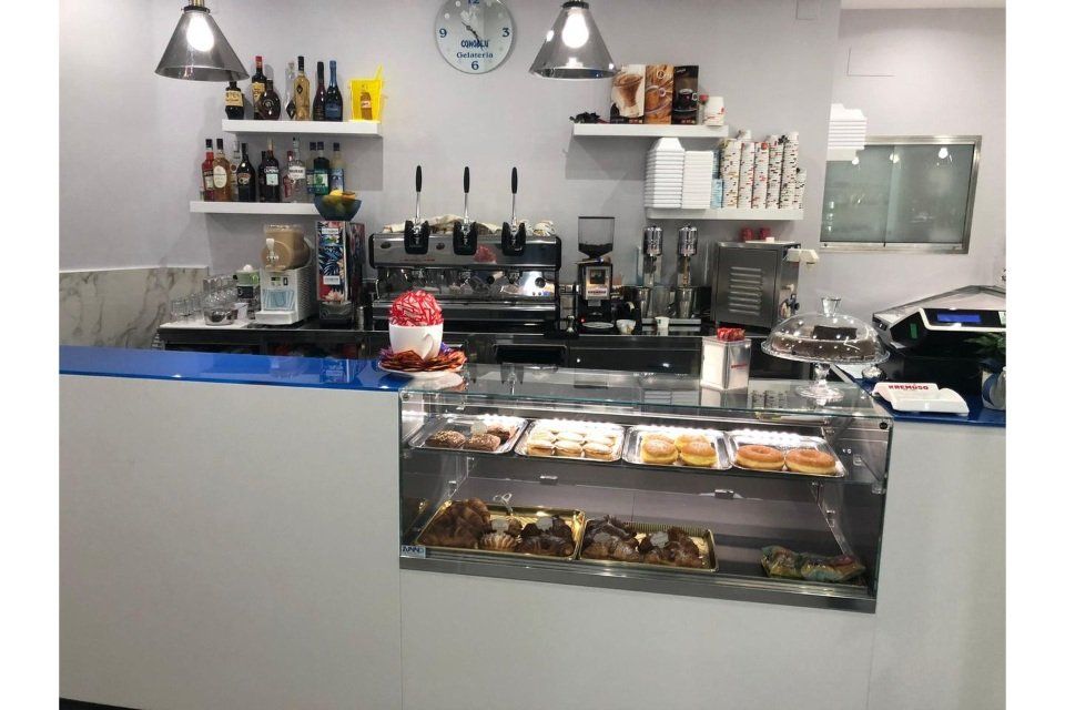 Bancone di una caffetteria con pasticcini, macchina per l'espresso e bottiglie sugli scaffali.