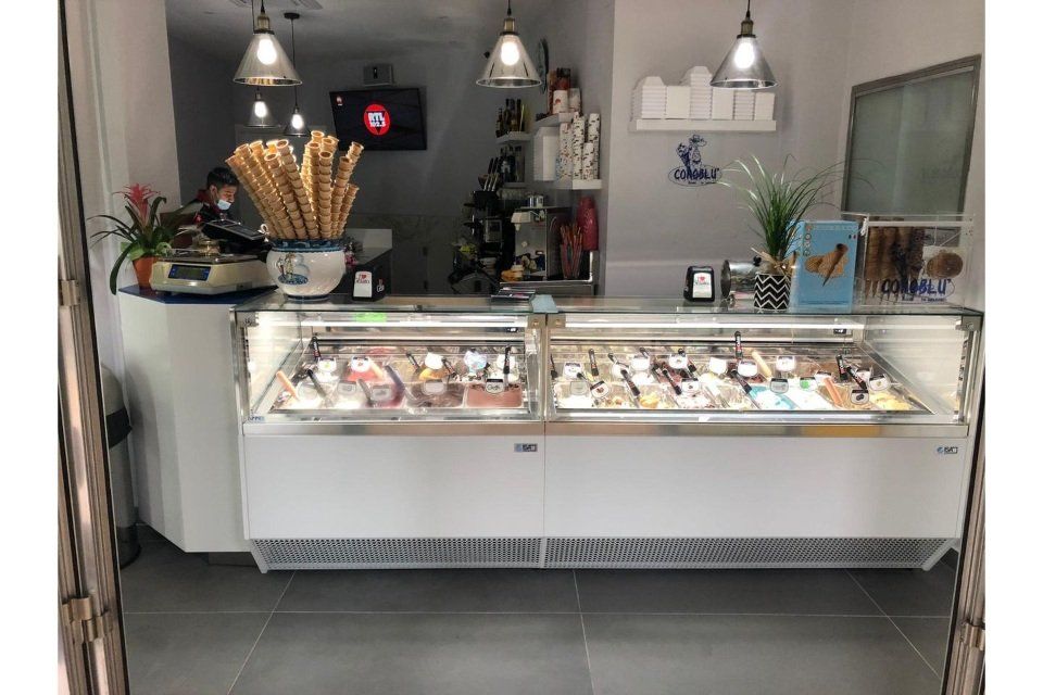 Interno di una gelateria con vetrina bianca, coni e gusti.