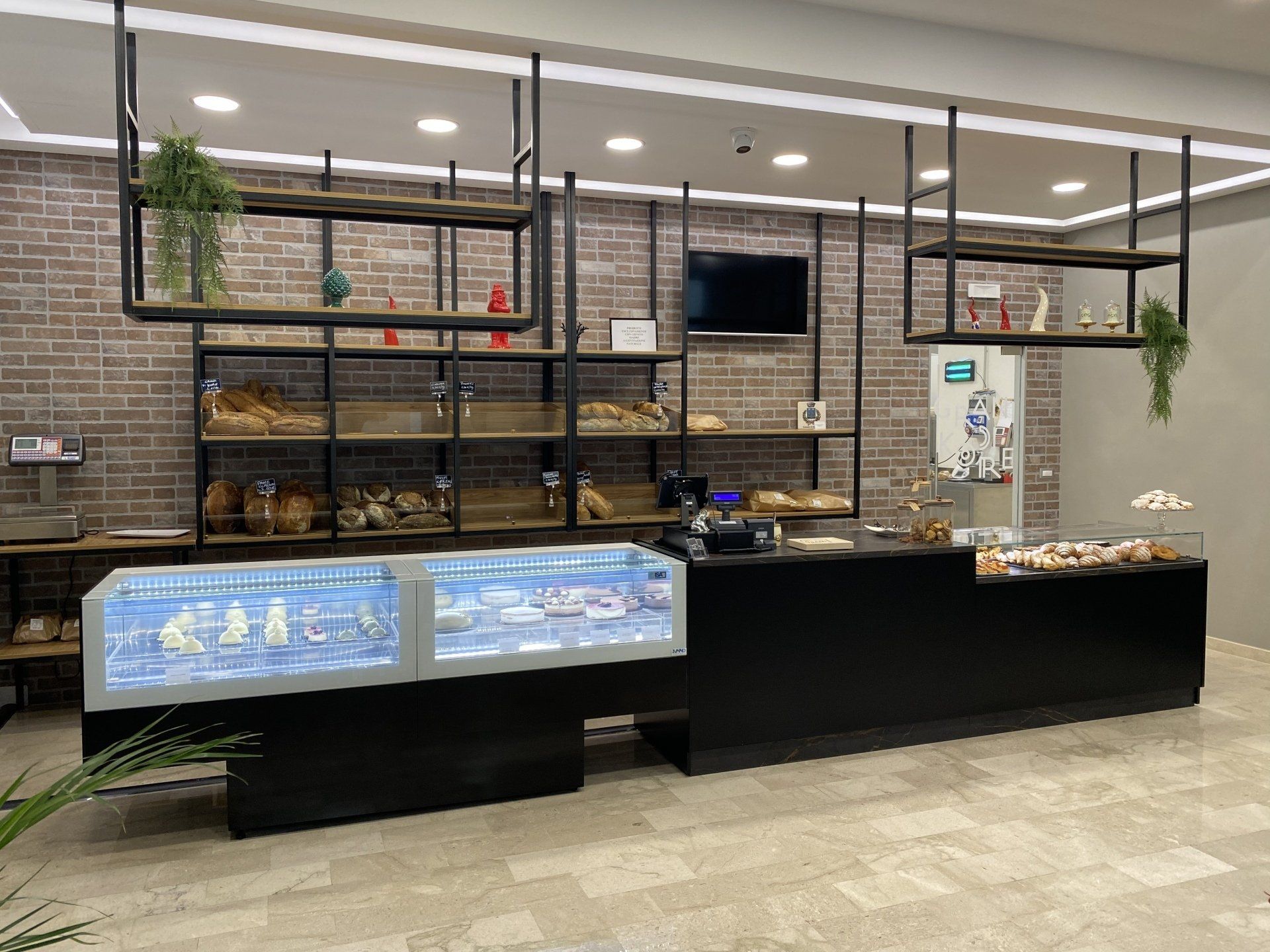 Interno di panetteria con vetrina, scaffali per il pane, bancone nero e ripiani sospesi.