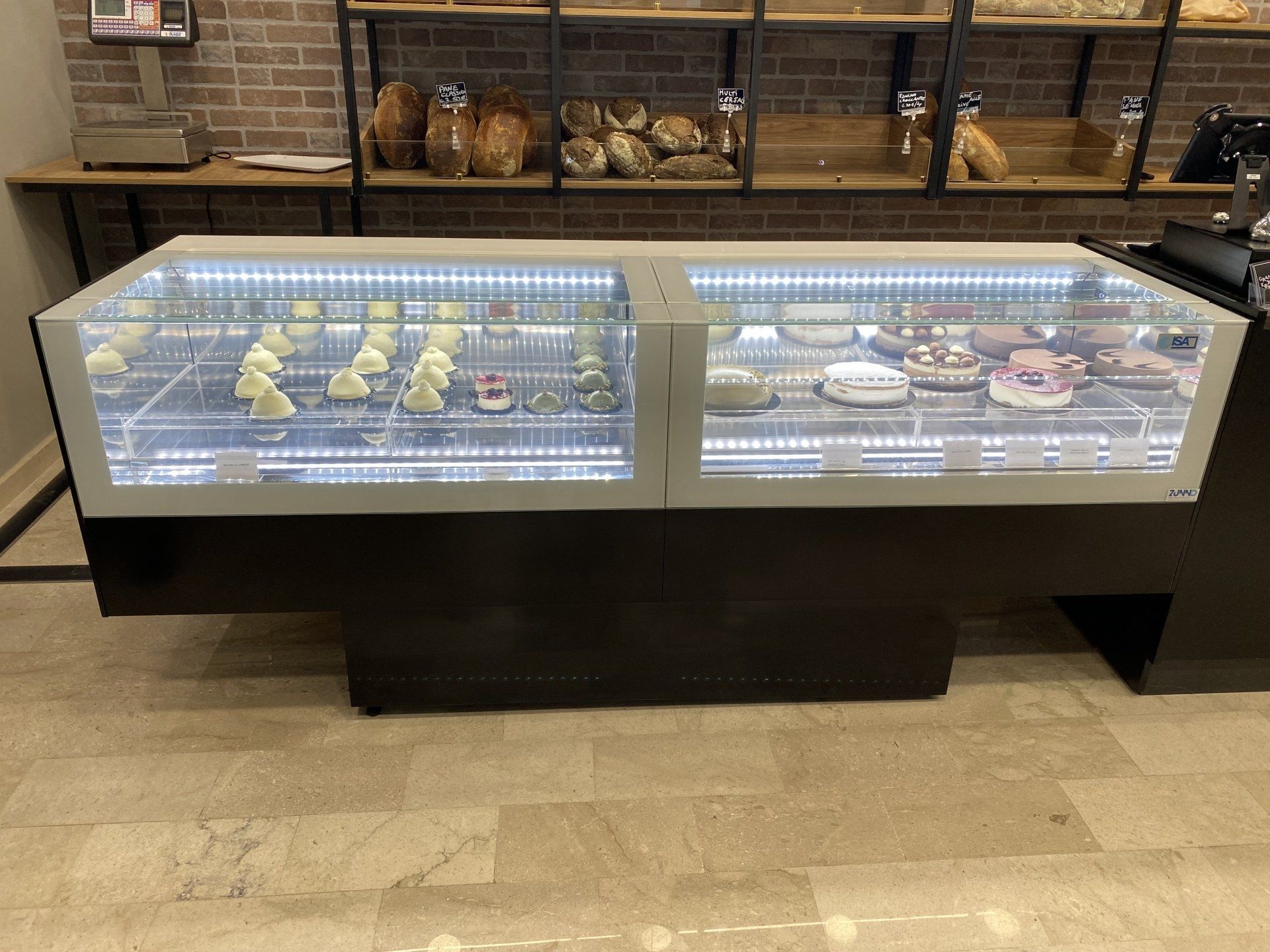 Una vetrina bianca e nera con dolciumi illuminata dall'alto in una panetteria.