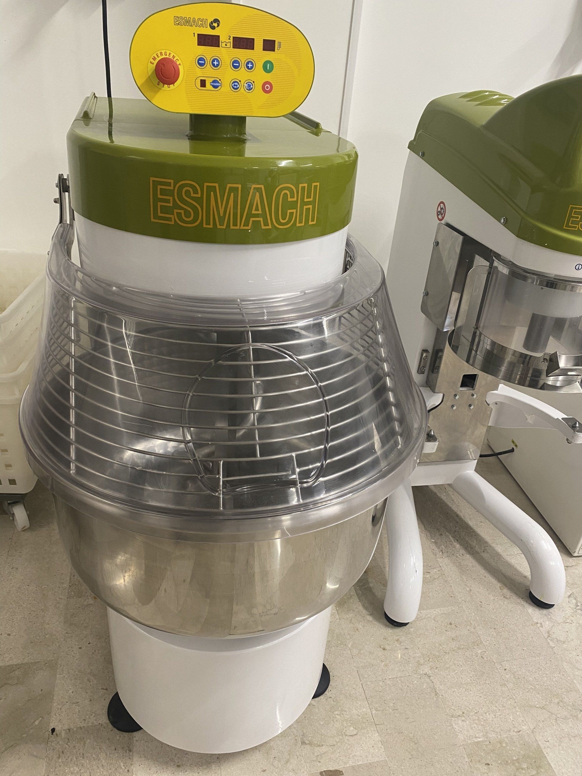 Un'impastatrice commerciale con una ciotola in acciaio inossidabile e una gabbia protettiva, accanto a un'altra macchina simile.