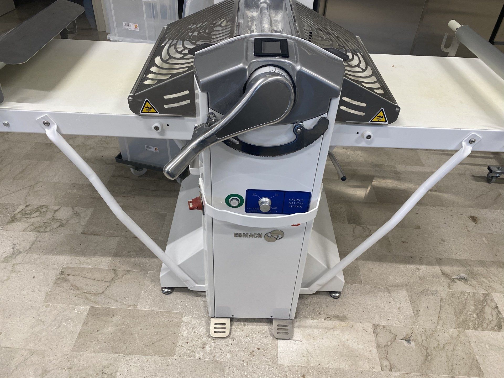 Sfogliatrice bianca per pasta da forno con maniglia e nastri trasportatori, su pavimento piastrellato.