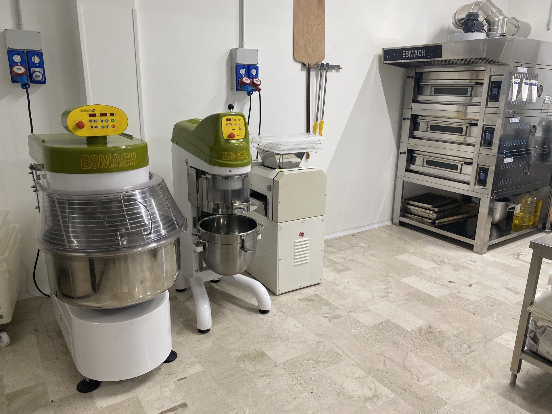 Attrezzatura da panetteria: grande impastatrice, planetaria e scaffalature in una stanza con pareti bianche.