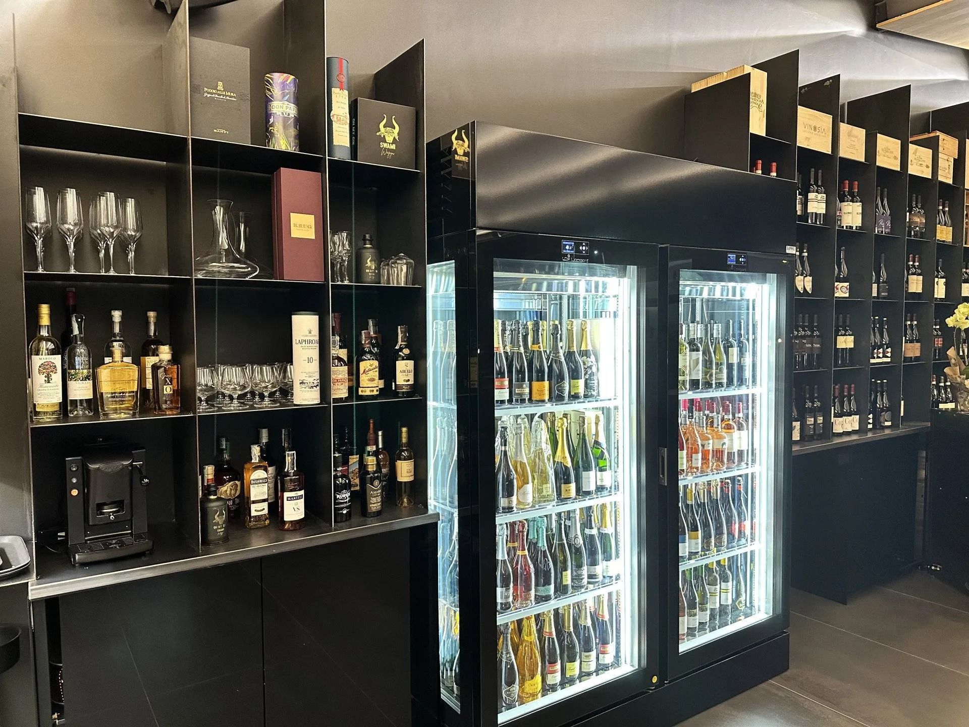 Un bar con scaffali pieni di bottiglie di liquore, bicchieri e un frigorifero a doppia porta pieno di bevande.