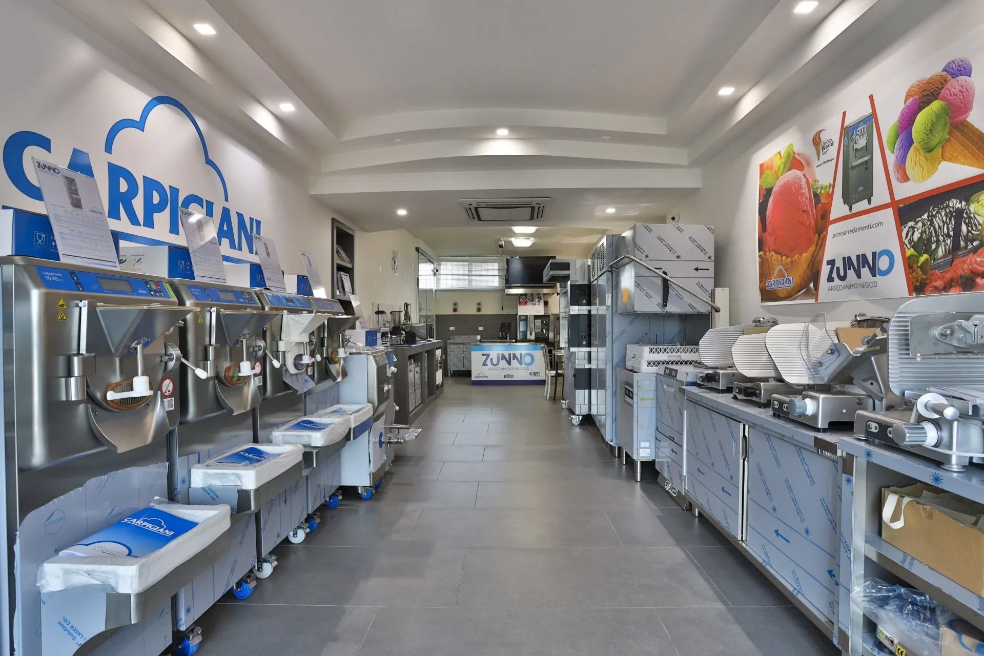 Interno di una cucina commerciale. File di macchine per il gelato, banconi e attrezzature in acciaio inox; un'insegna Carpigiani.