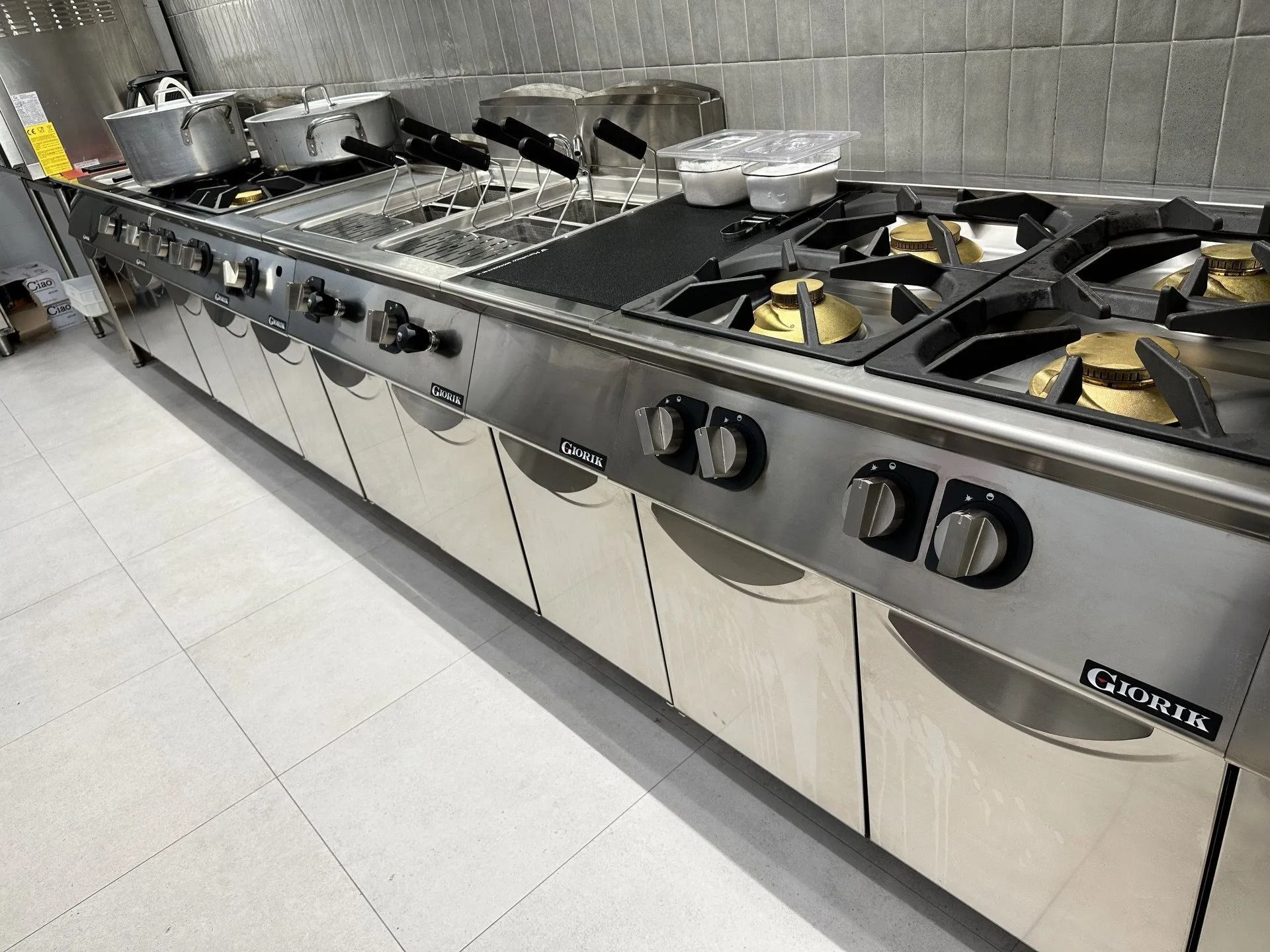 Cucina commerciale in acciaio inox con più fuochi e superfici di cottura.