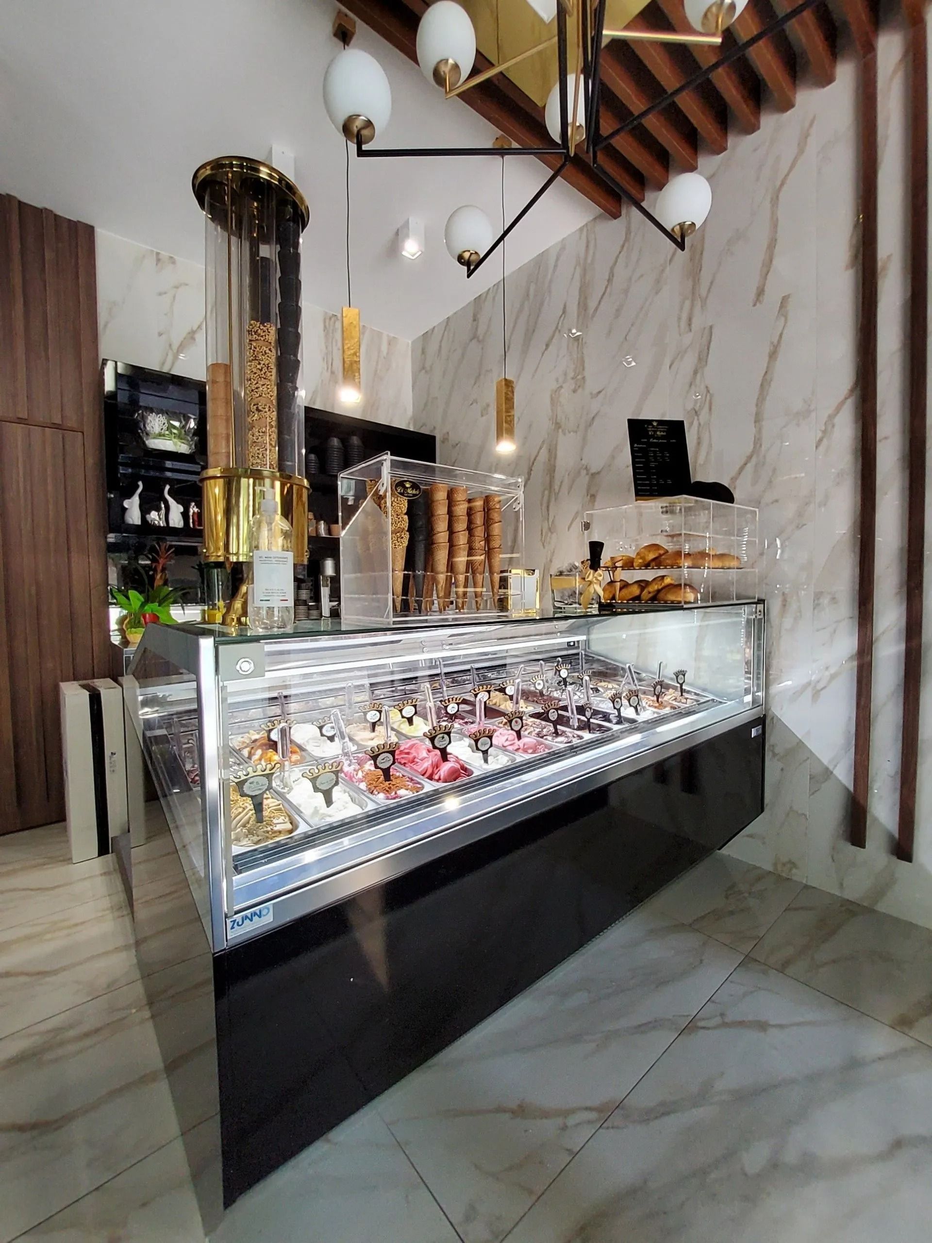 Interno di una gelateria con vetrina di gelato, luci decorative e pareti in marmo.