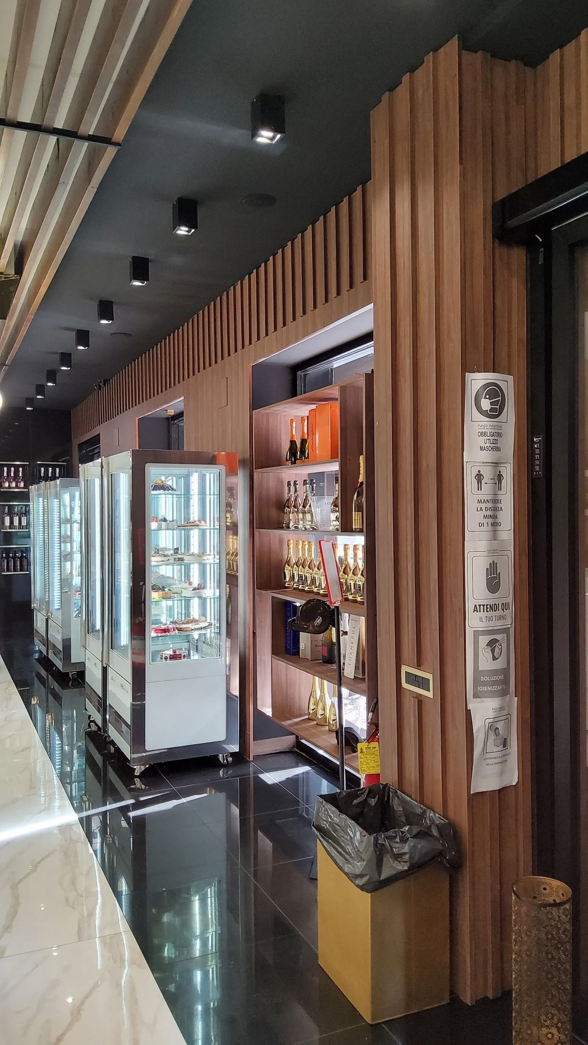 L'interno di un negozio con vetrine in vetro, scaffali in legno con bottiglie e pavimento nero.